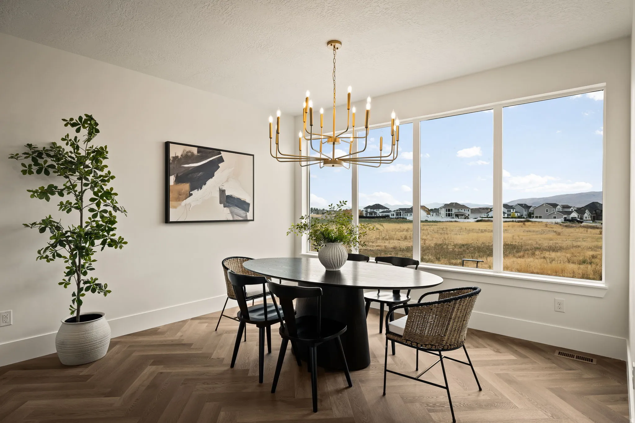 Dining area featuring a modern brass chandelier, large windows, and wood-finish flooring with a herringbone pattern