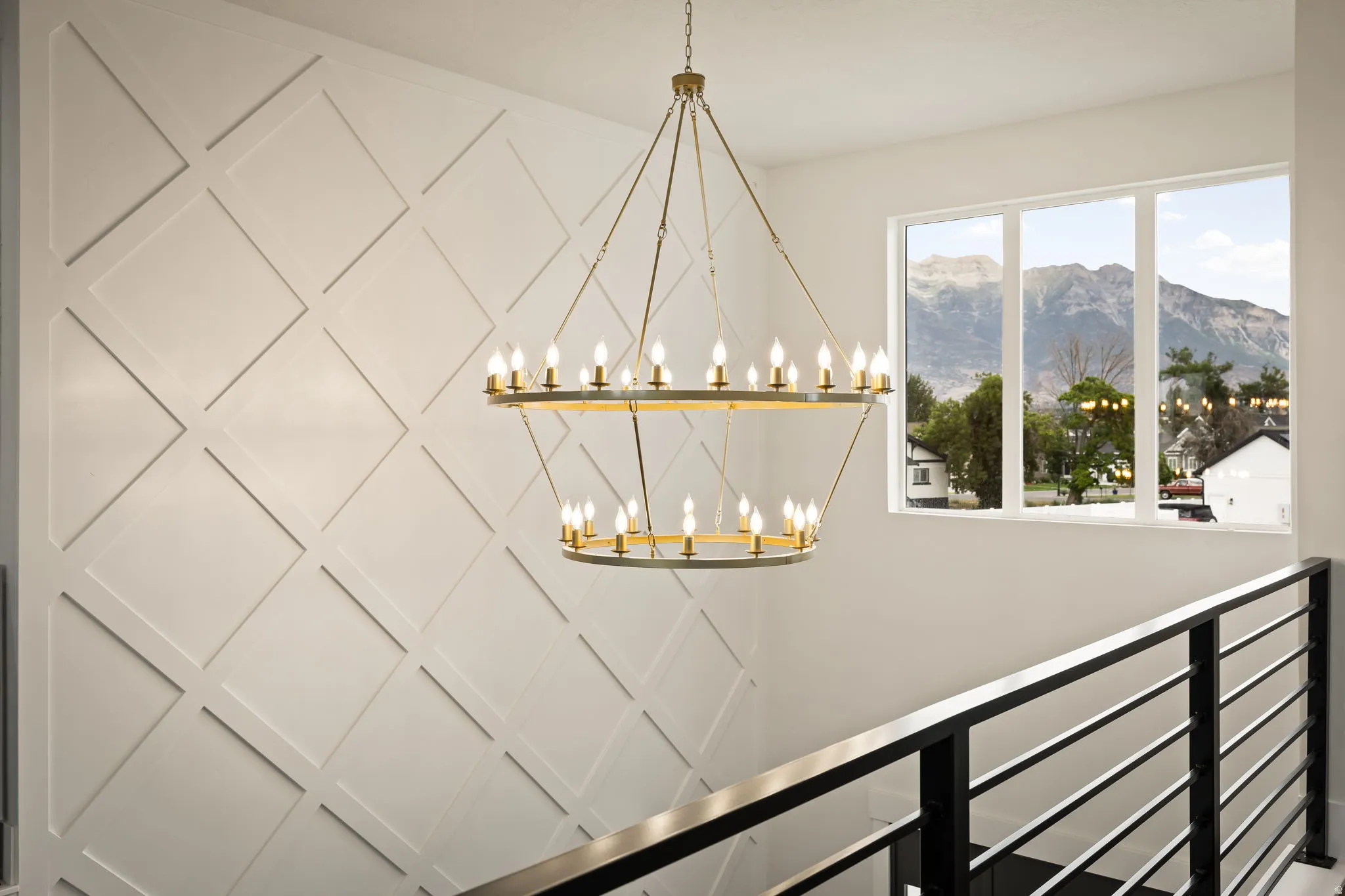 Stairwell featuring a two-tiered chandelier, geometric accent wall paneling, a large window with mountain scenery, and contemporary black metal railings