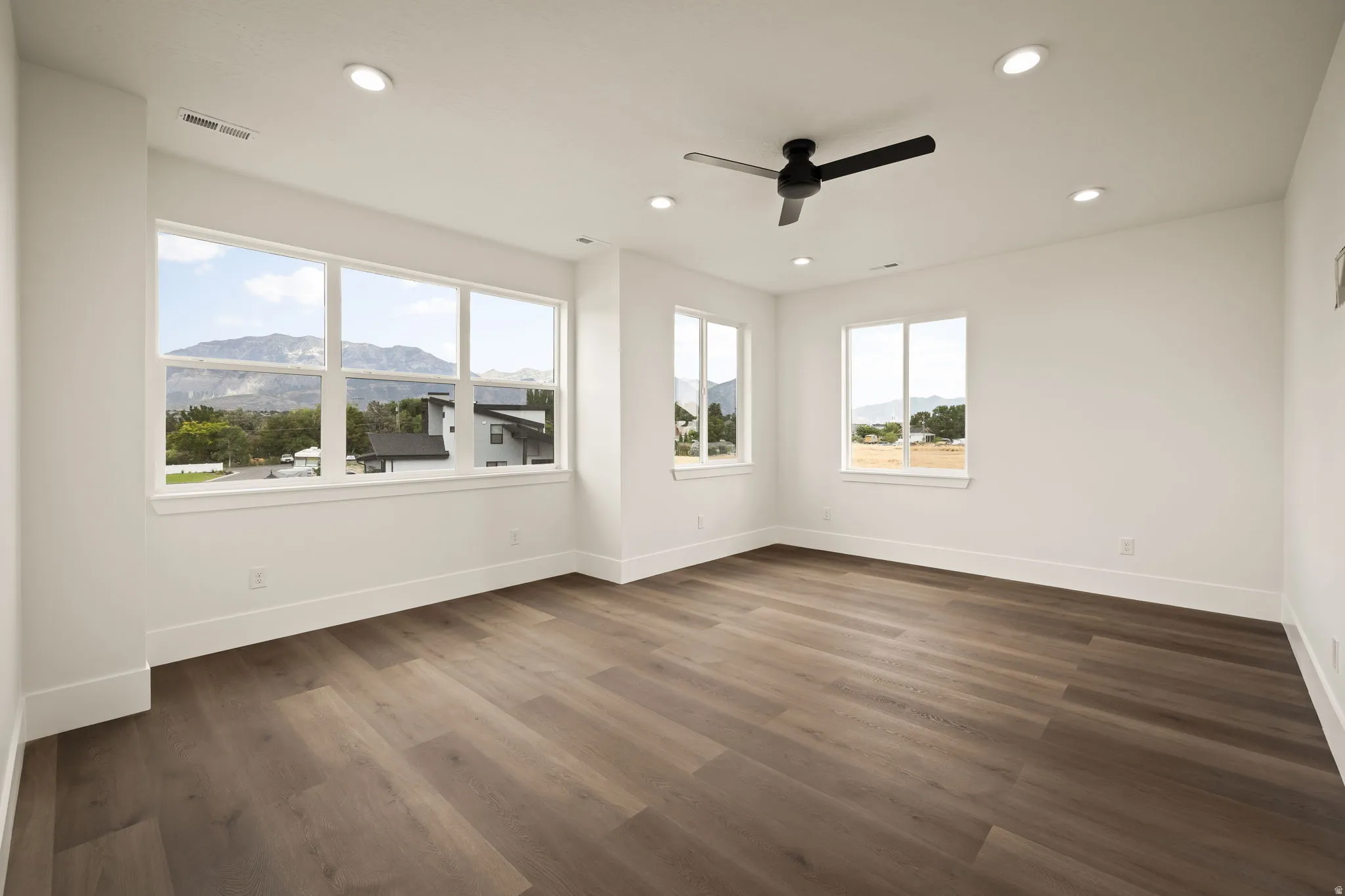 Expansive room featuring wood-finish flooring, multiple windows, a ceiling fan, and recessed lighting