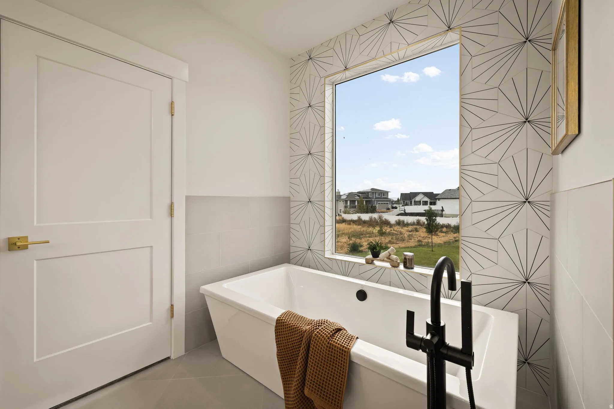 Freestanding soaking tub with a floor-mounted matte black faucet, set against a geometric tiled accent wall