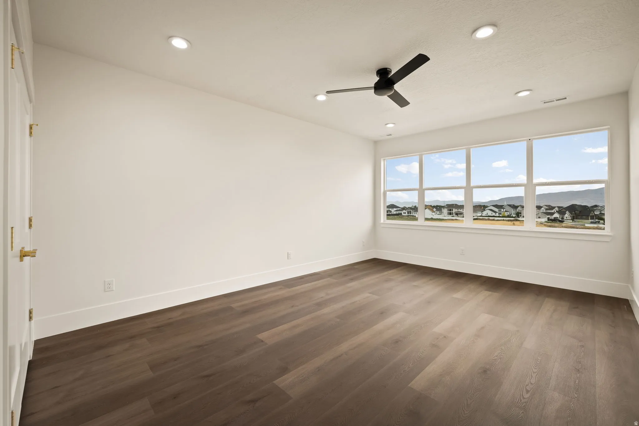 Spacious room featuring wood-finish flooring, a contemporary ceiling fan, and recessed lighting