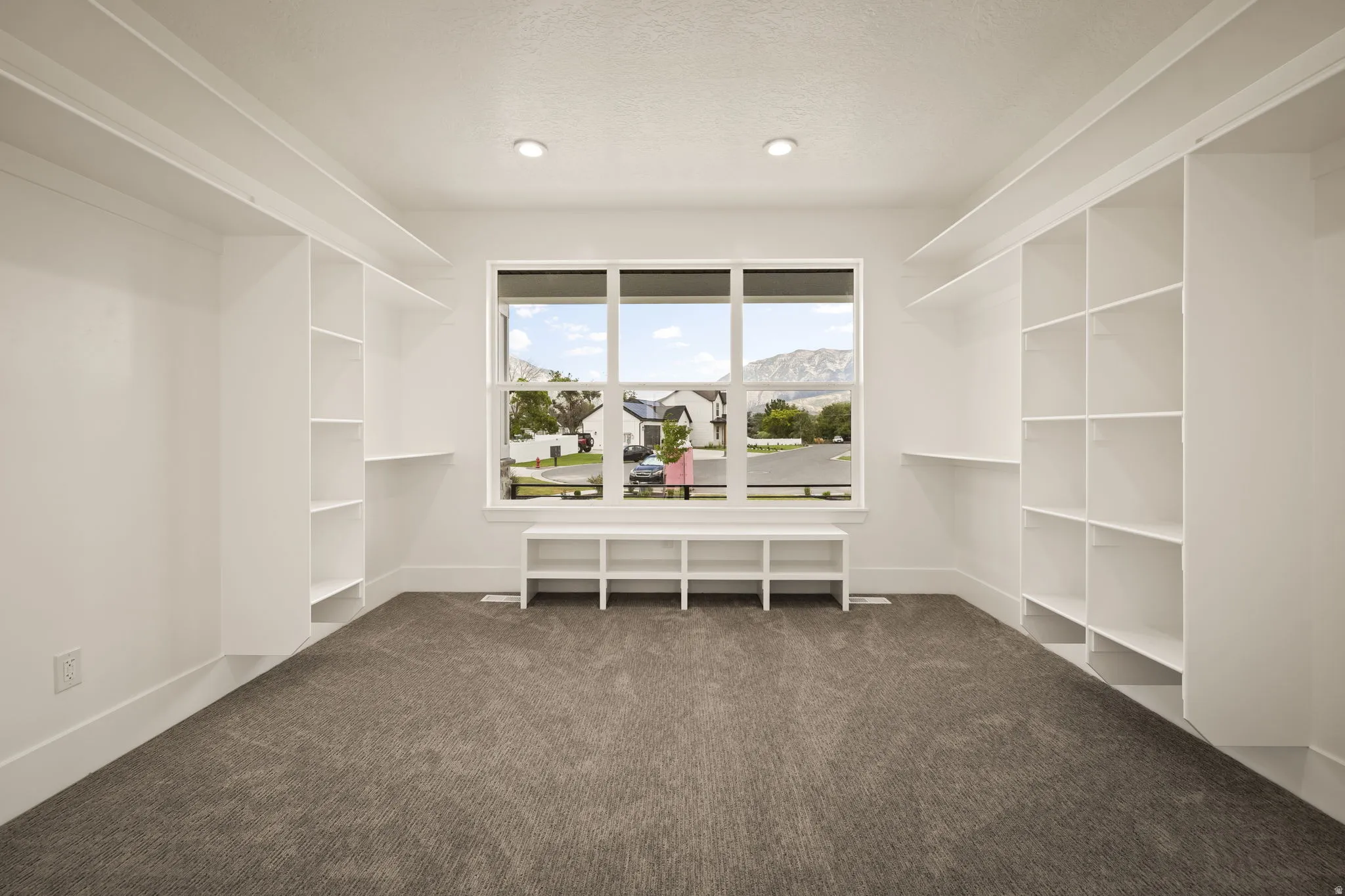 Spacious interior featuring built-in shelving, plush carpet flooring, a large window, recessed lighting, and a built-in window bench