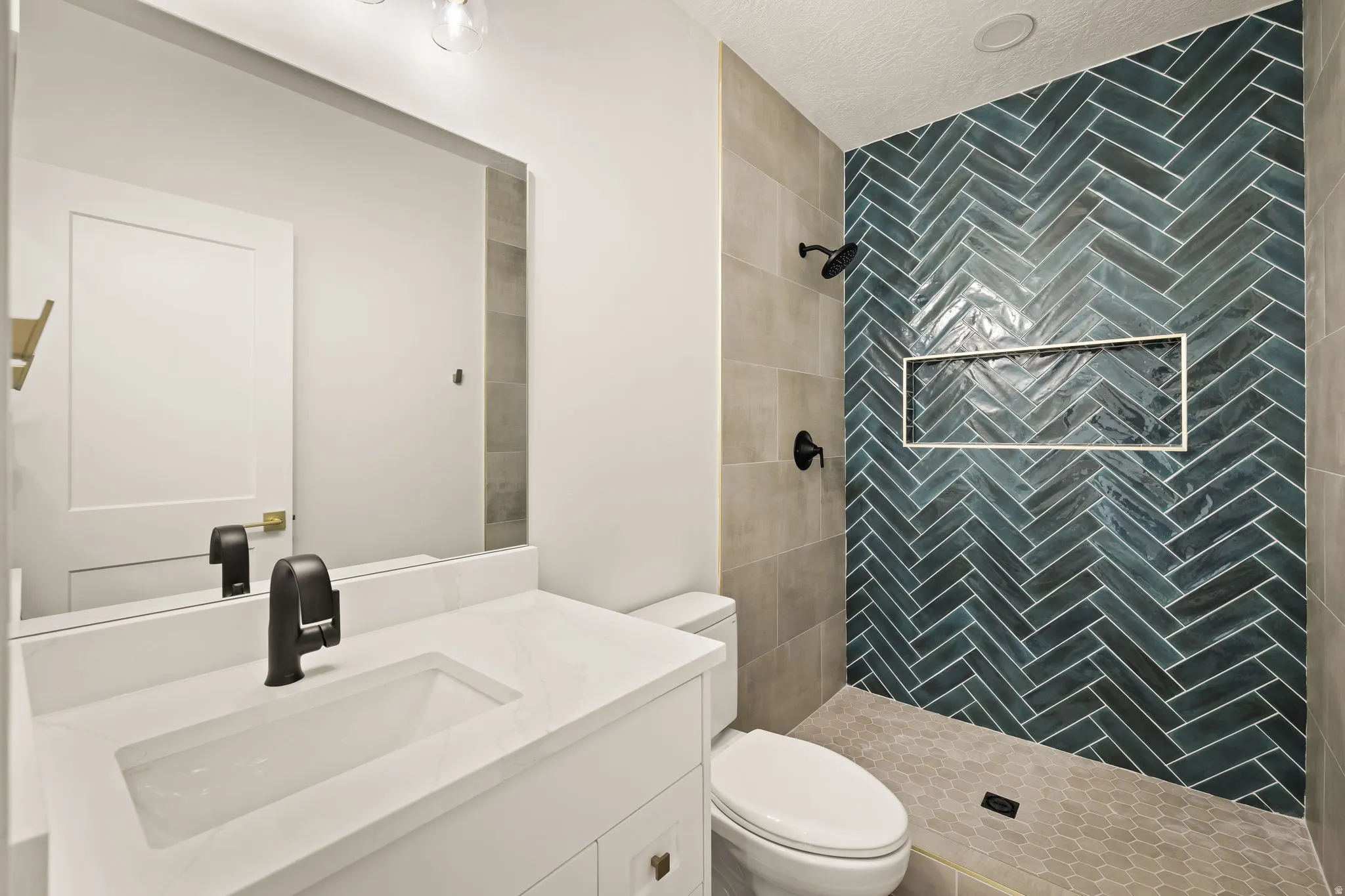 Walk-in shower featuring a herringbone tile accent wall, built-in niche, and dark bronze fixtures