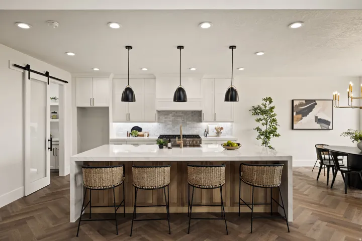 Kitchen featuring a large island with a light-toned countertop, pendant lighting, herringbone wood-finish flooring, white cabinetry, and a tile backsplash