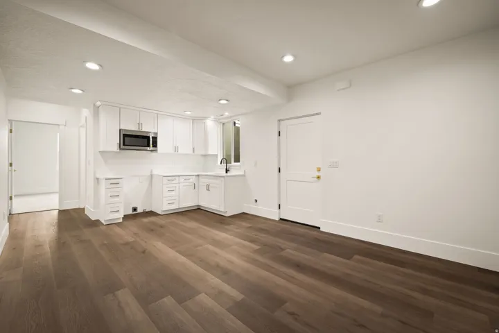 Open concept space featuring a corner kitchen with white shaker cabinetry, an undermount sink, and stainless steel microwave