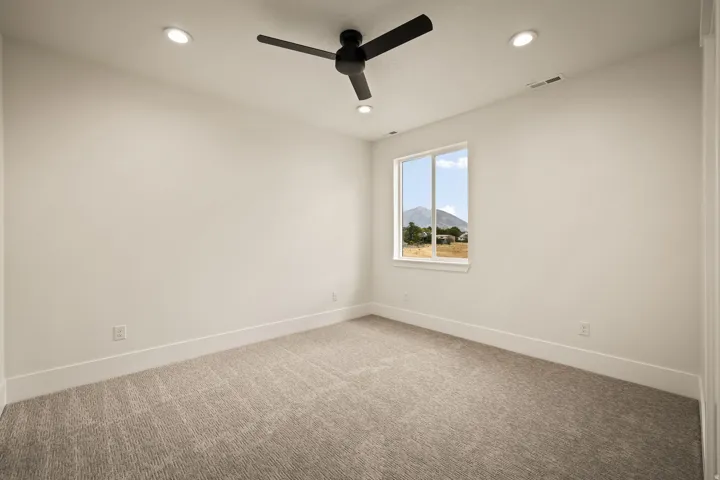 Neutral-toned carpeted room featuring a ceiling fan with integrated lighting, recessed ceiling lights, and a window framing a distant mountain landscape