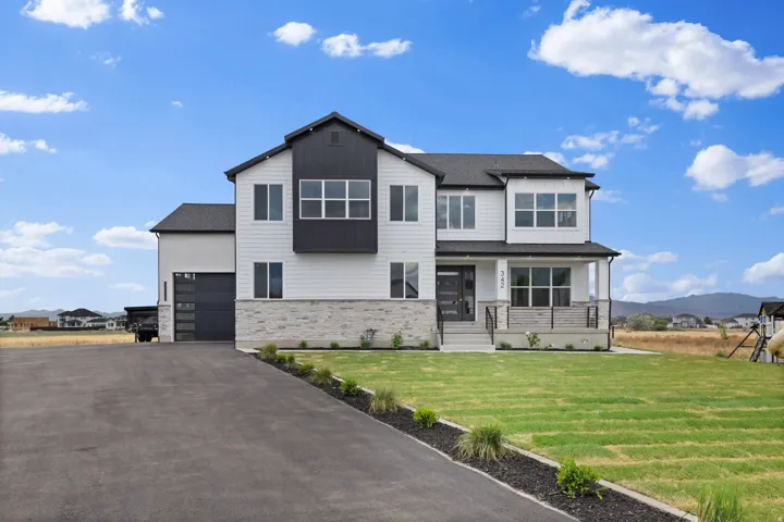 Modern two-story residence featuring white siding, dark trim accents, stone foundation elements, a covered front porch with railing, and a paved driveway