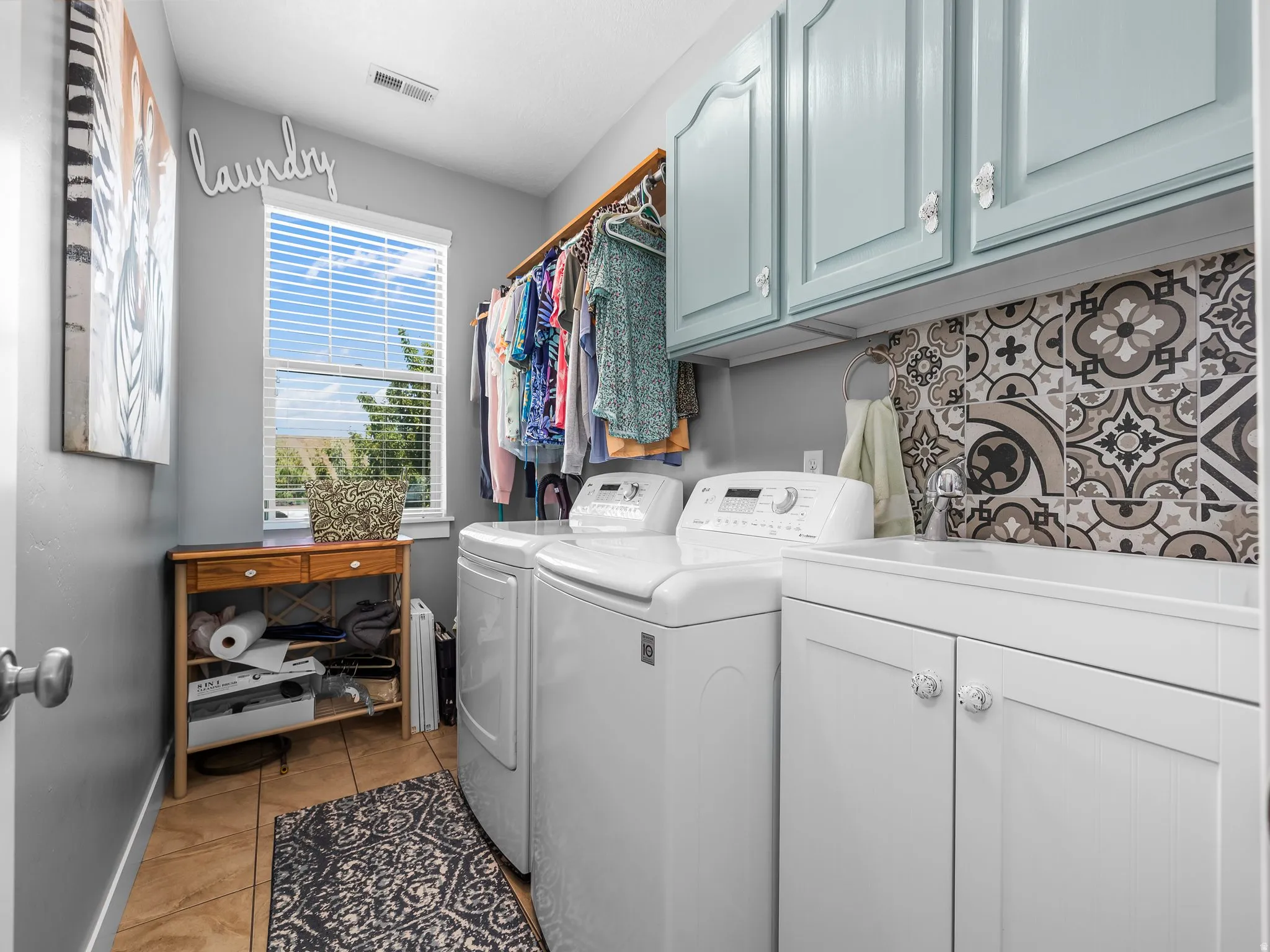 Dedicated laundry room featuring light blue upper cabinetry, white lower cabinetry with integrated sink, and an ornamental tile backsplash