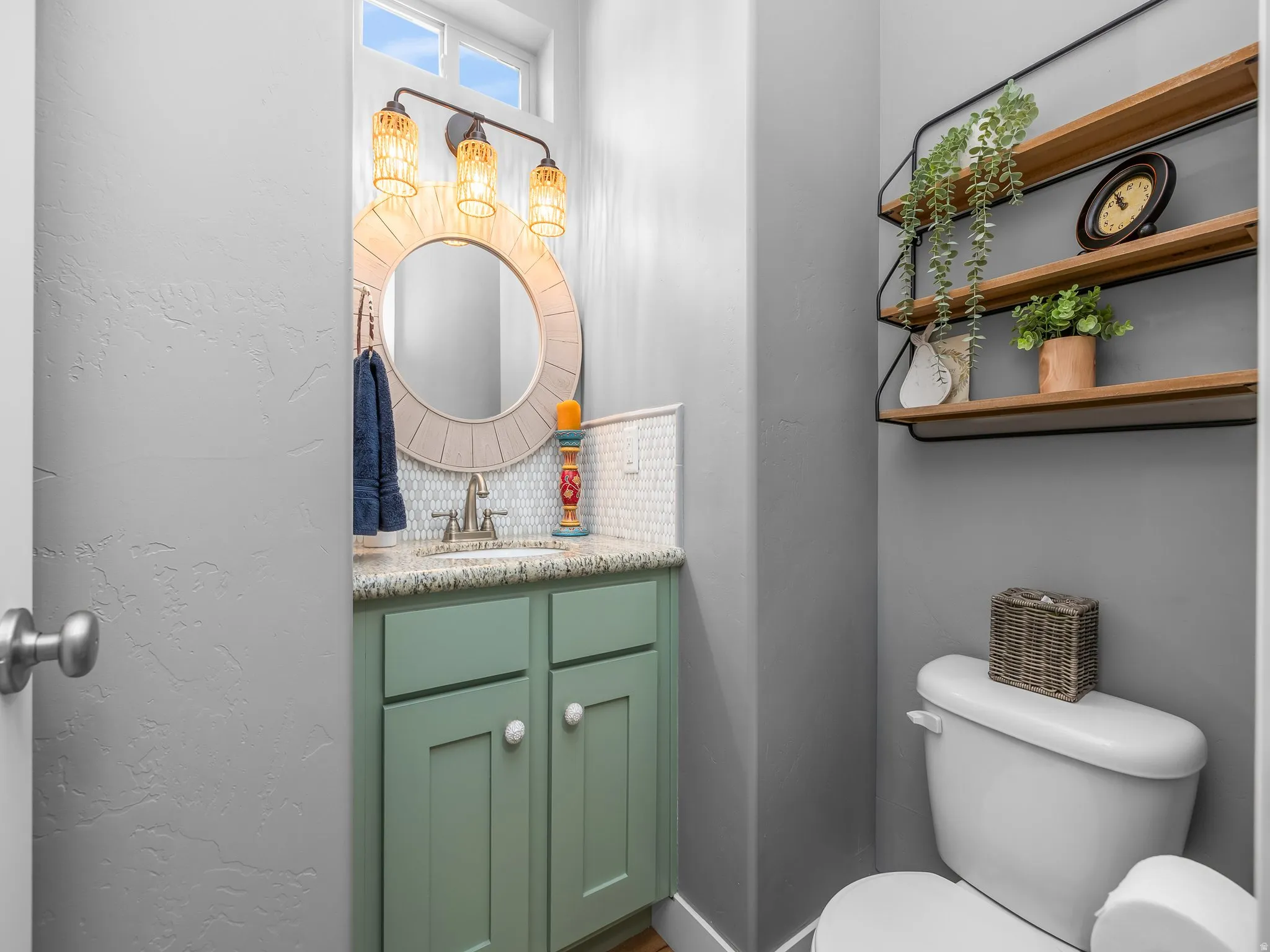 Bathroom featuring a sage green vanity with a granite-style countertop, a circular mirror, and a three-light fixture