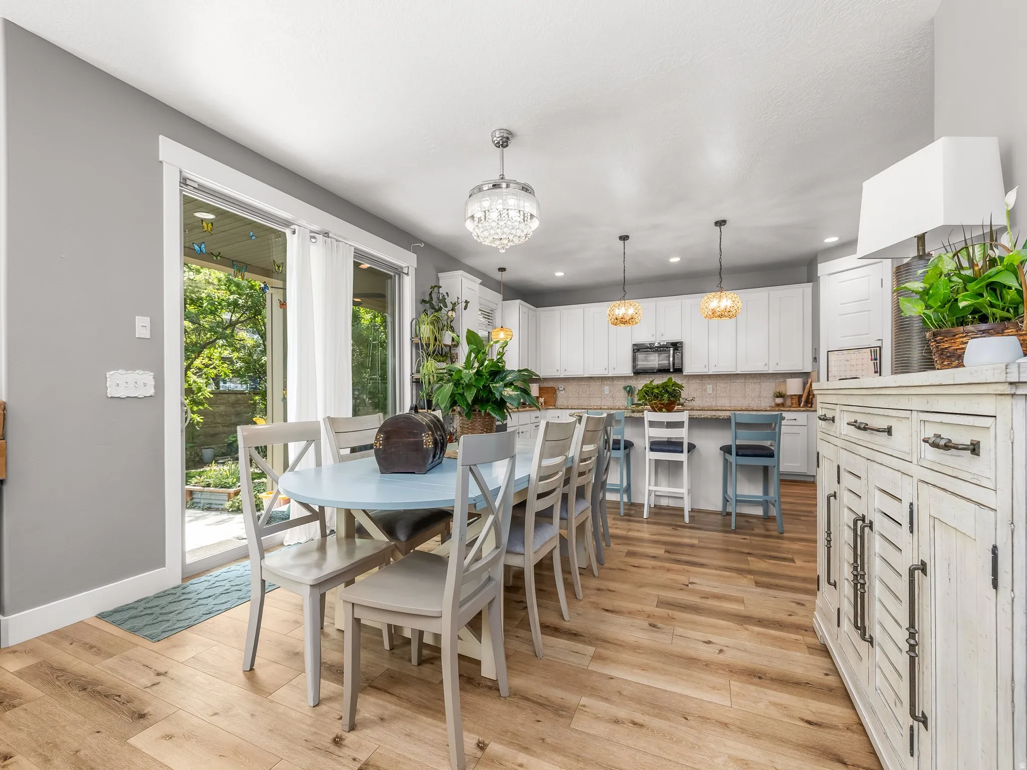 Open-concept dining and kitchen area featuring wood-finish flooring, white cabinetry, a kitchen island with seating, a crystal chandelier, and sliding glass doors to the exterior