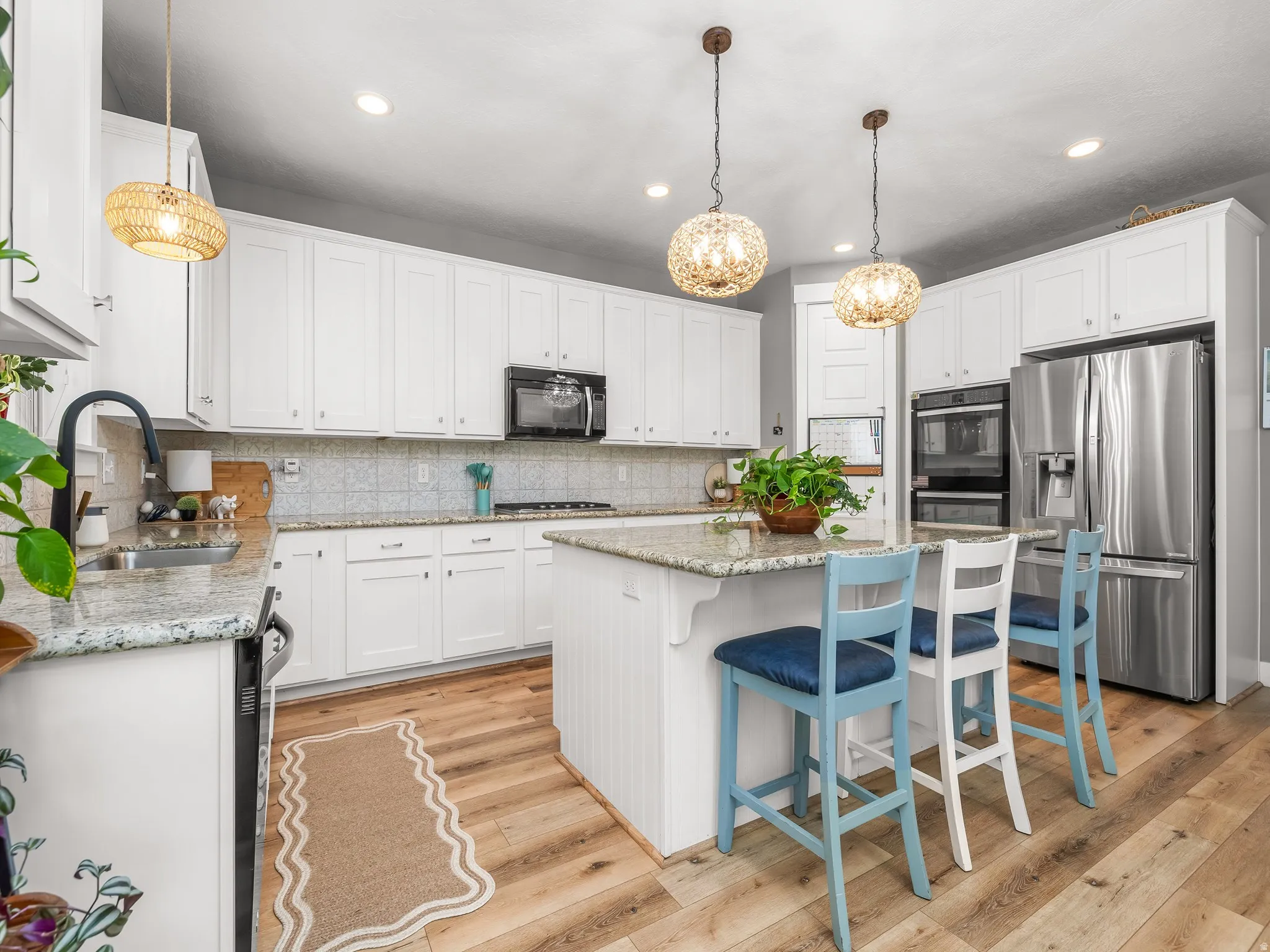 Spacious kitchen featuring extensive white cabinetry, granite countertops, stainless steel appliances, wood-finish flooring, and a central island with pendant lighting