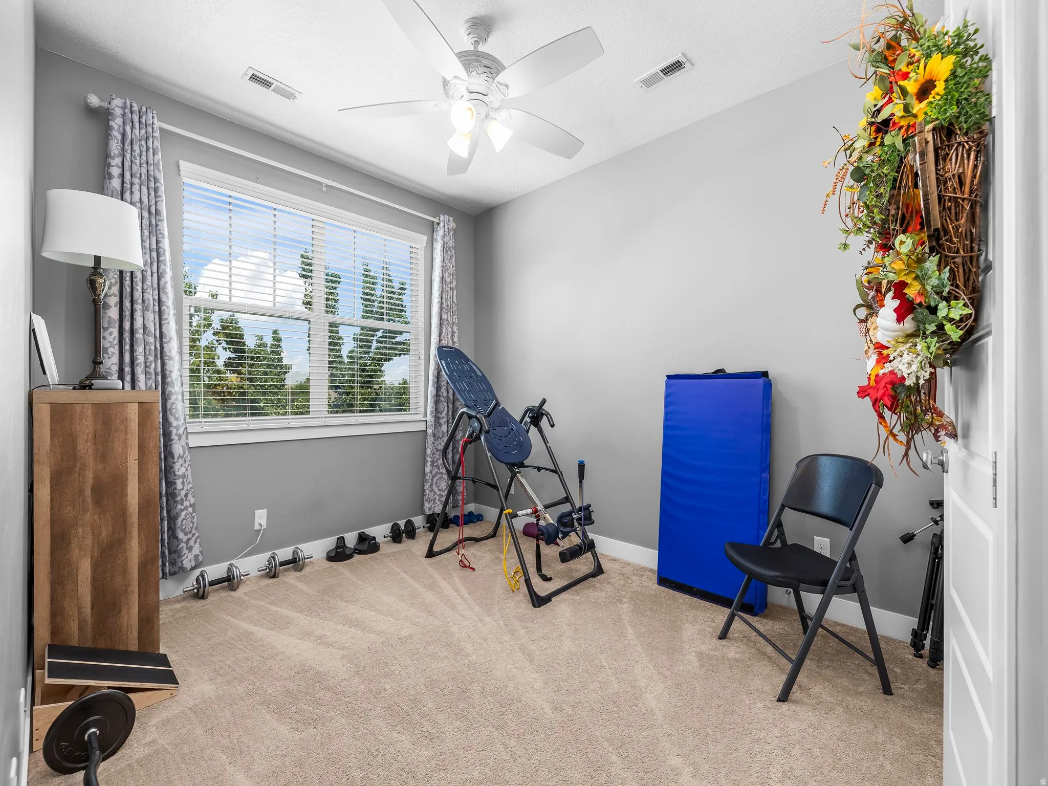 Versatile bonus room with bright natural light from large multi-pane windows, ceiling fan with integrated lighting, neutral carpeting, and white walls
