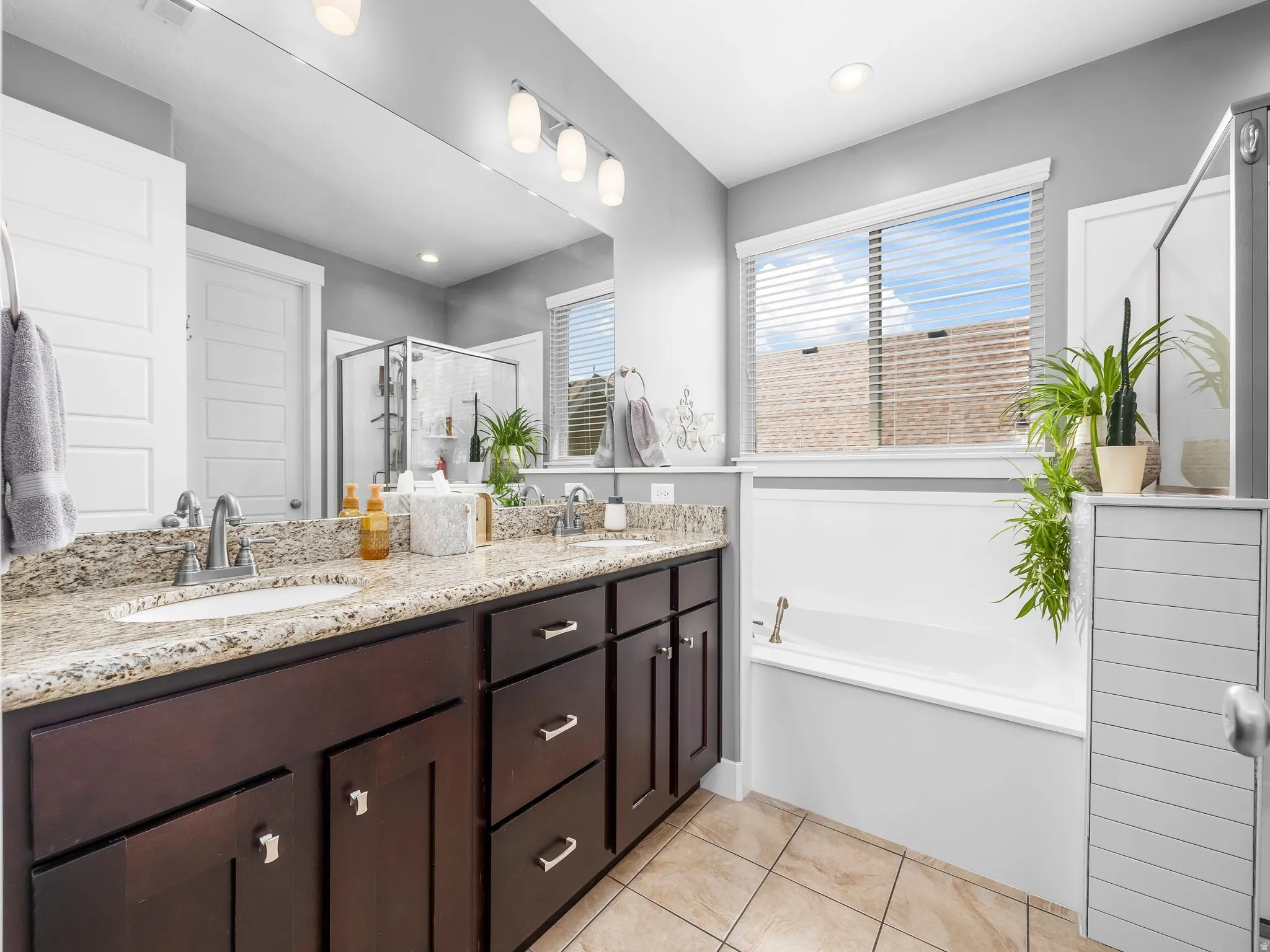Spa-inspired primary bathroom featuring a dark wood vanity with dual sinks, granite countertops, and polished chrome fixtures