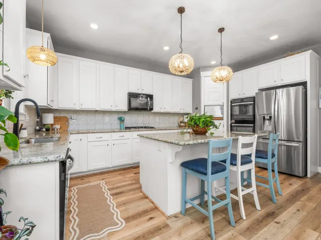 Spacious kitchen featuring extensive white cabinetry, granite countertops, stainless steel appliances, wood-finish flooring, and a central island with pendant lighting