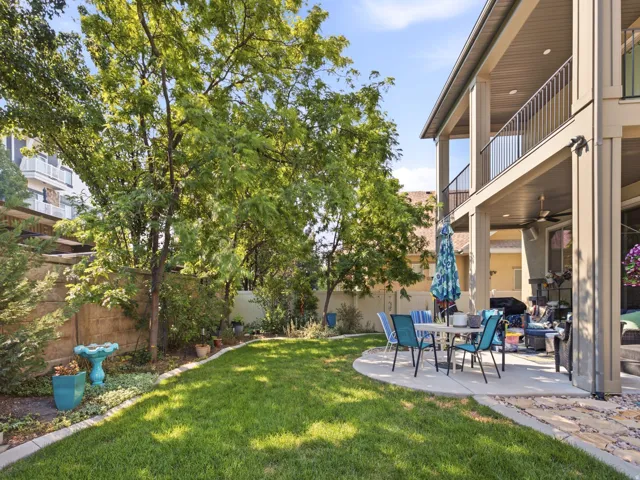 Spacious backyard featuring a manicured lawn, concrete patio, and mature trees