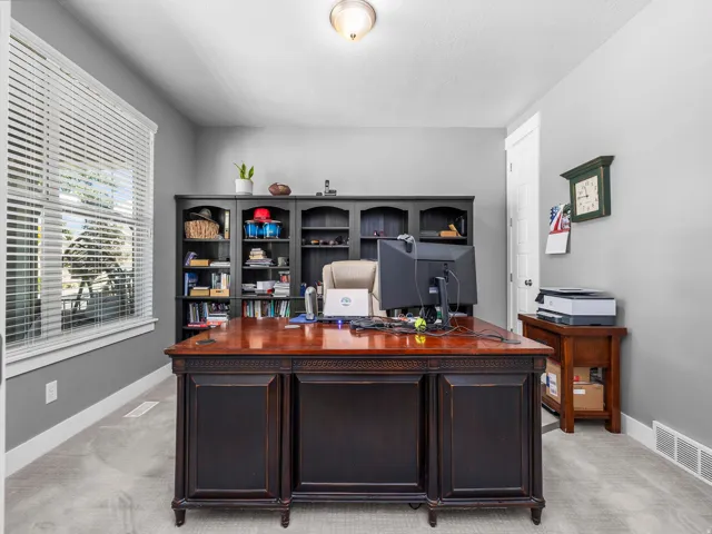 Dedicated room featuring light gray wall paint, carpeting, a ceiling-mounted light fixture, a large window with white blinds, and built-in shelving