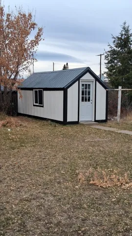 Exterior storage building featuring a dark metal roof, white siding, black trim, a white entry door with glass panes, and a single window