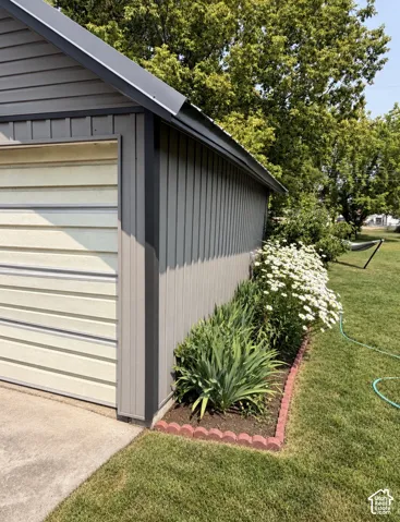 Side-gabled structure with vertical siding, metal roof, and a low-maintenance landscape bed featuring mature plantings