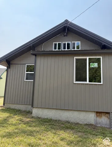Gable roof with dark trim, vertical panel siding, and multiple windows
