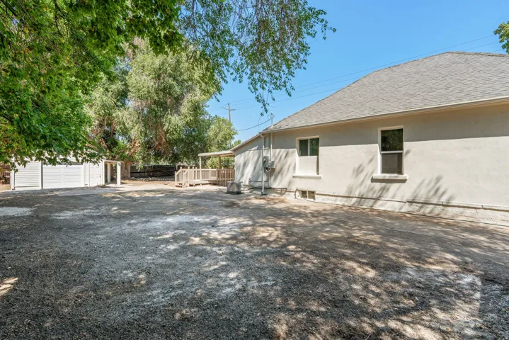 Spacious gravel yard featuring a stucco exterior, a large wood deck, and an outbuilding with double doors