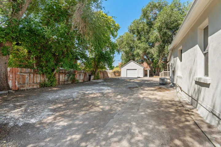 Spacious exterior area featuring a detached garage with a white roll-up door, a white stucco main building, and mature trees providing natural shade