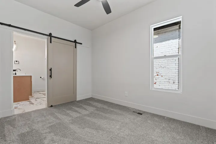Room featuring light gray patterned carpet, a single window, and a ceiling fan
