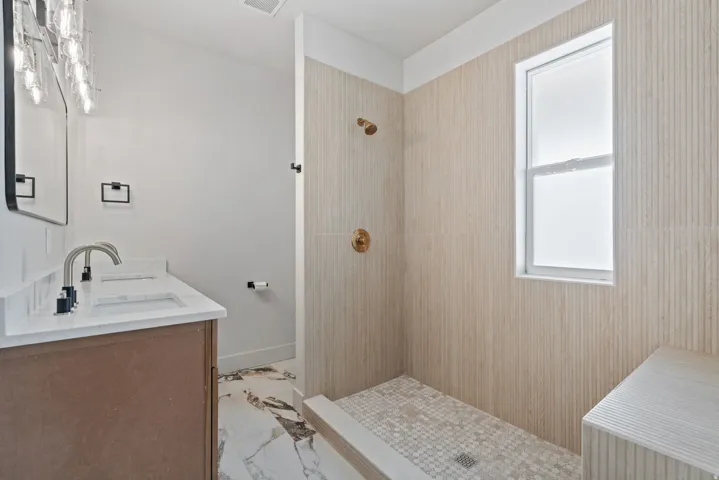 Walk-in shower featuring vertically-oriented textured tile, a built-in bench, and a gold-finish shower system