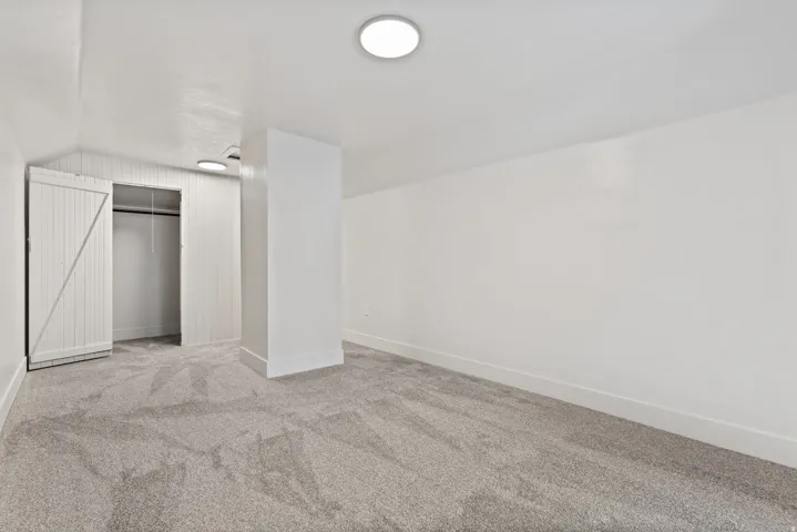 Carpeted room featuring a barn door closet with hanging rod, a white structural column, recessed lighting, and white baseboards