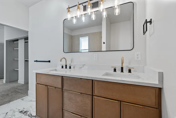 Dual vanity featuring wood-finish cabinetry with gold-tone hardware, white marble-look countertops, and integrated sinks