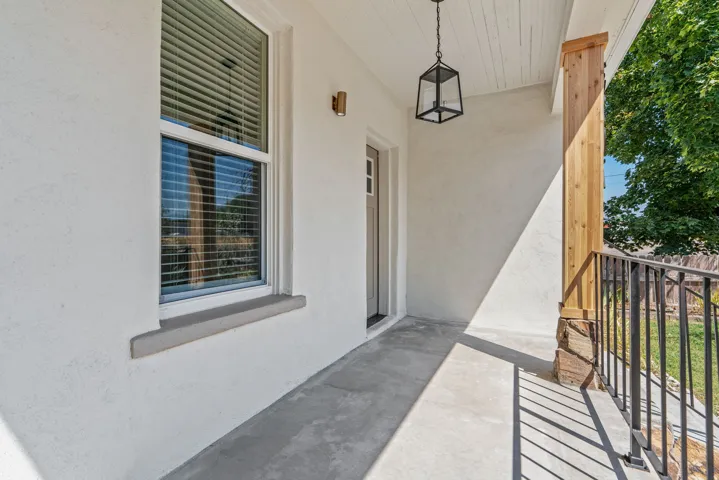 Inviting front porch featuring a white stucco exterior, concrete flooring, and a decorative black lantern light fixture