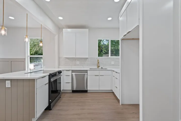 Modern kitchen featuring white cabinetry, stainless steel appliances, a white tile backsplash, and light wood-finish flooring