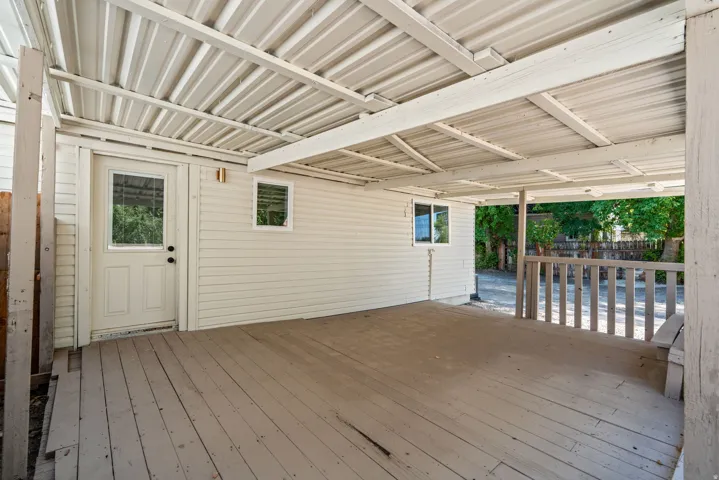 Covered outdoor deck featuring wood-finish flooring, white siding, a single entry door with window, and two additional windows
