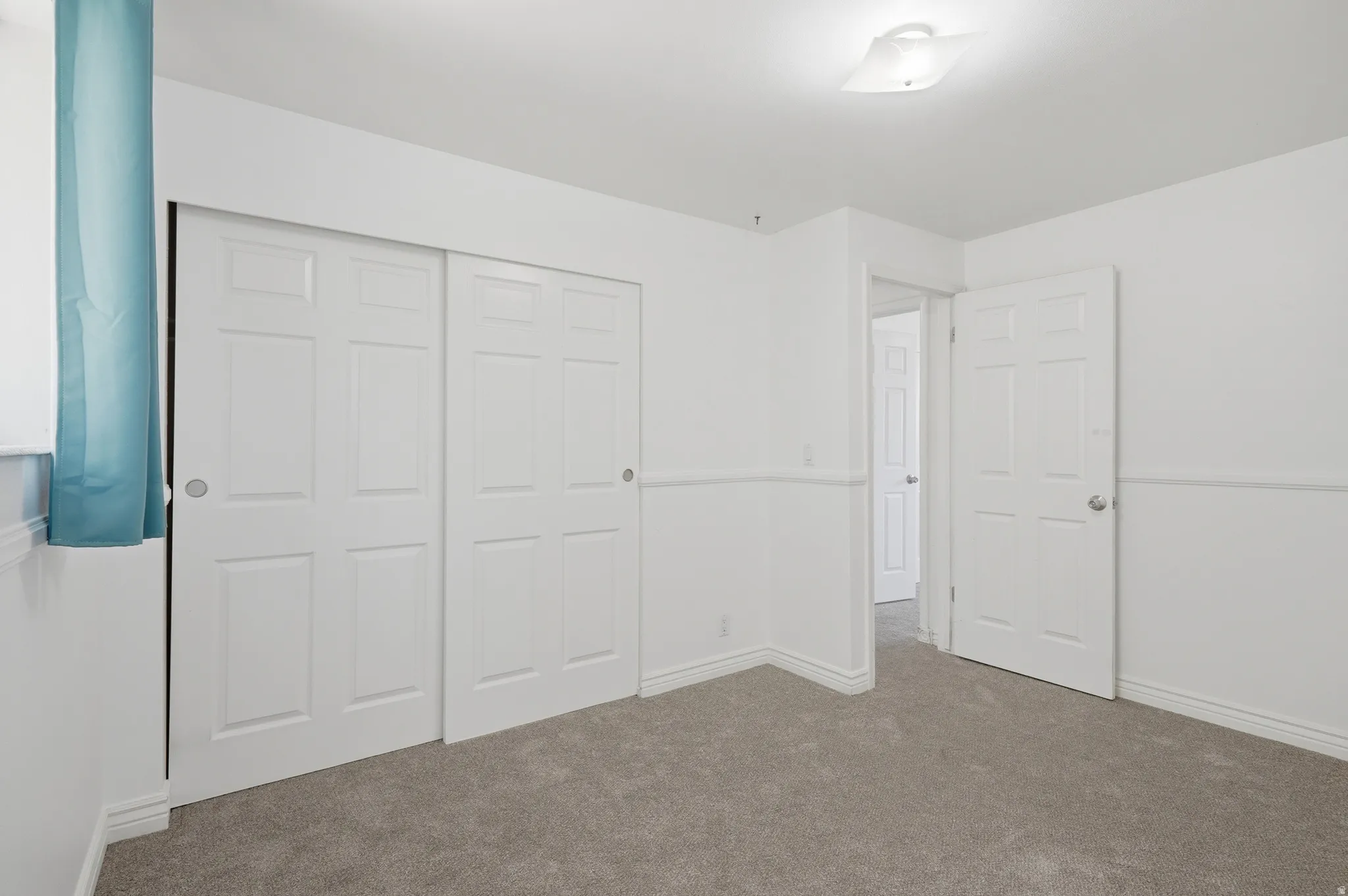 Spacious room featuring neutral carpet flooring, white walls with wainscoting detail, and a flush mount ceiling light