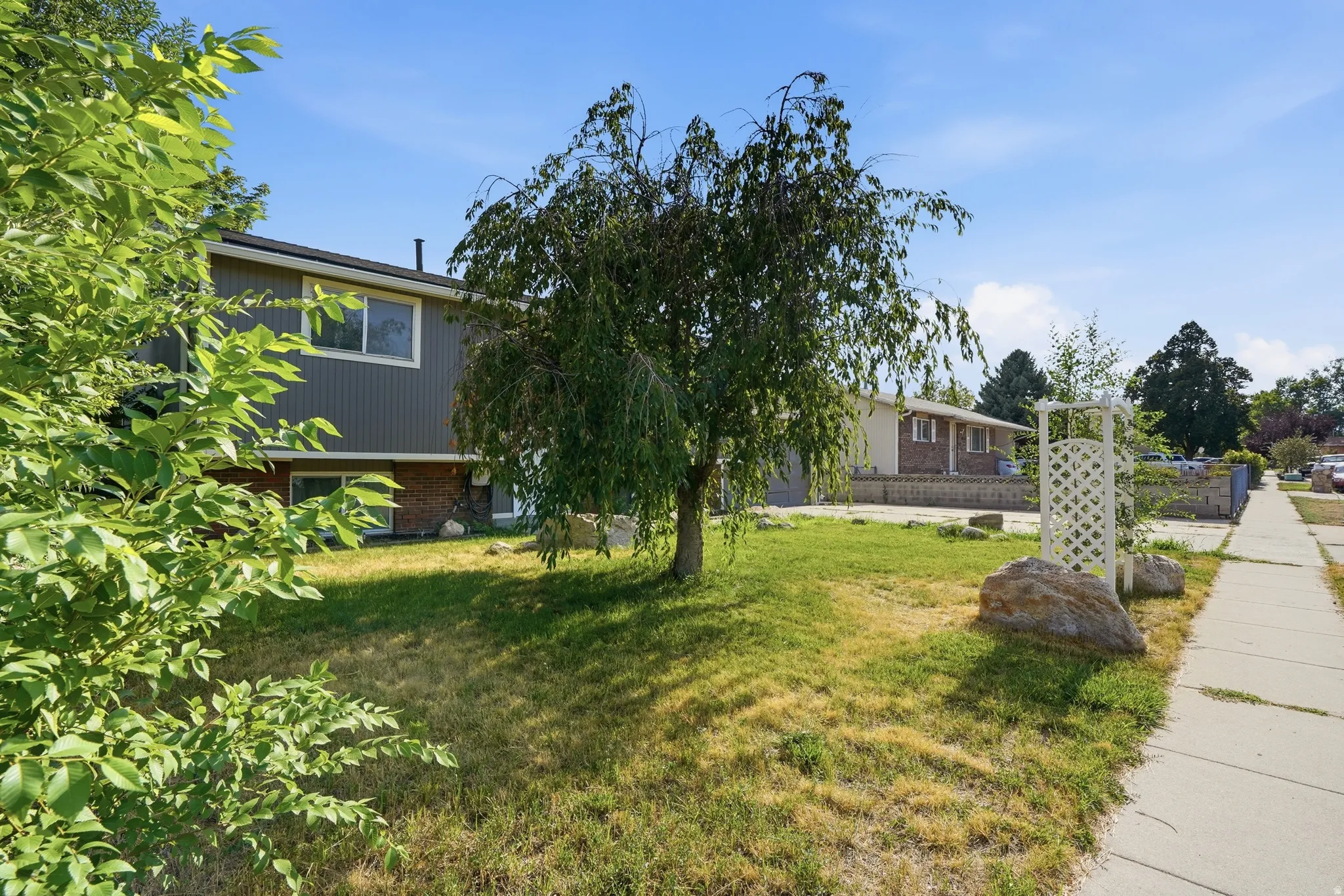 Split-level residence featuring gray vertical siding and a brick base