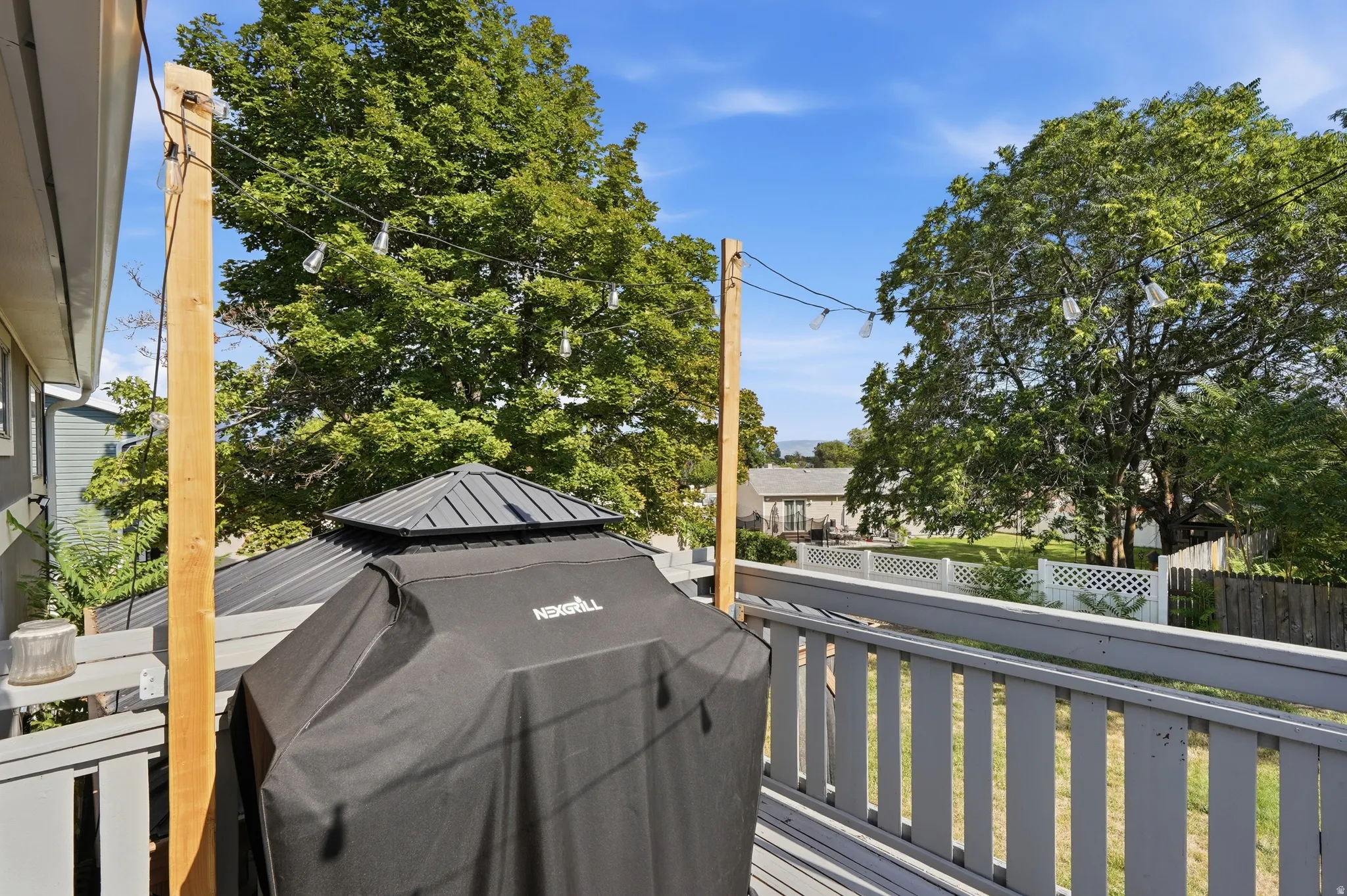 Spacious deck with painted wood railing, string lighting, and mature trees providing natural shade