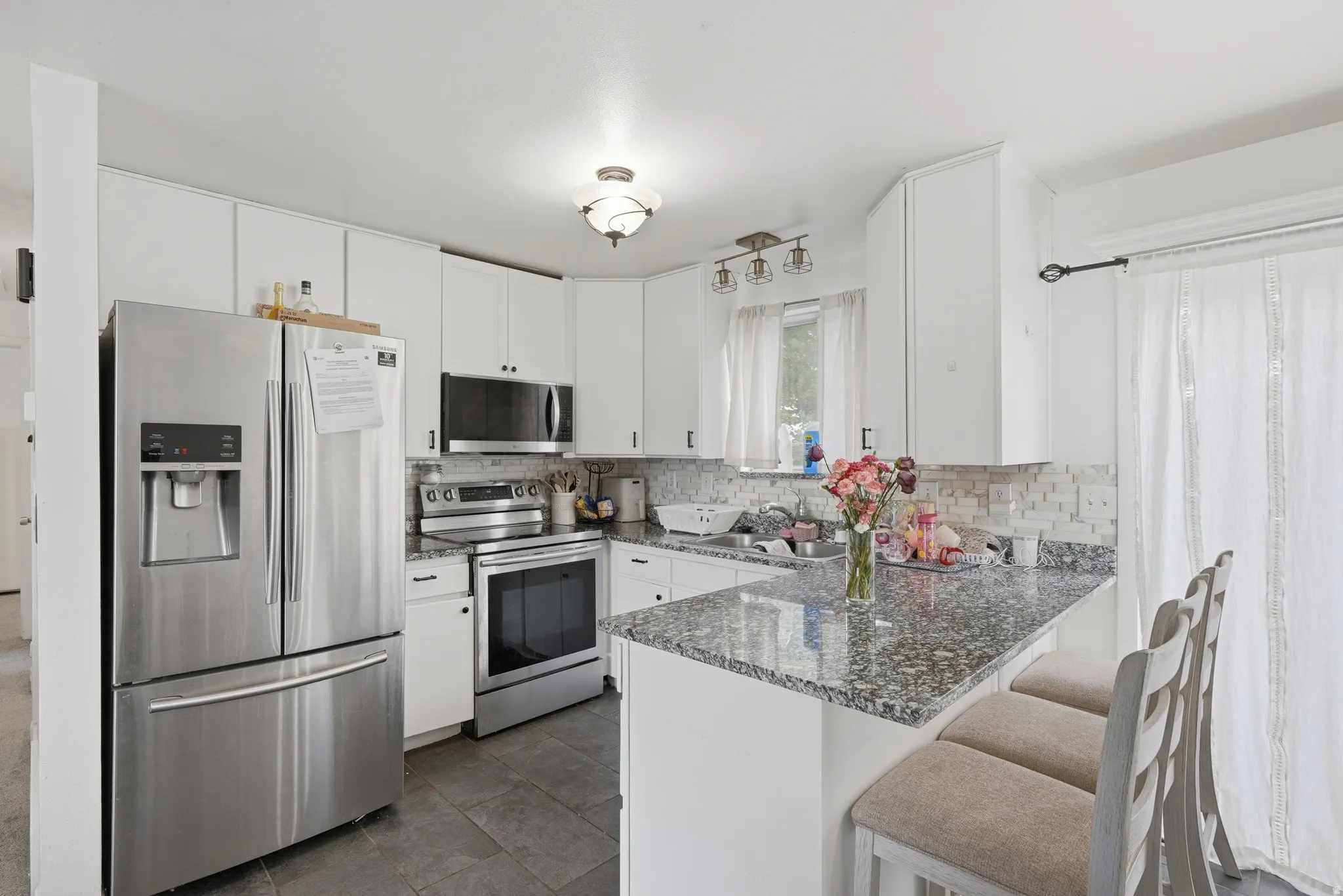 Kitchen featuring white cabinetry, stainless steel appliances, speckled countertops, a tile backsplash, and dark tile flooring