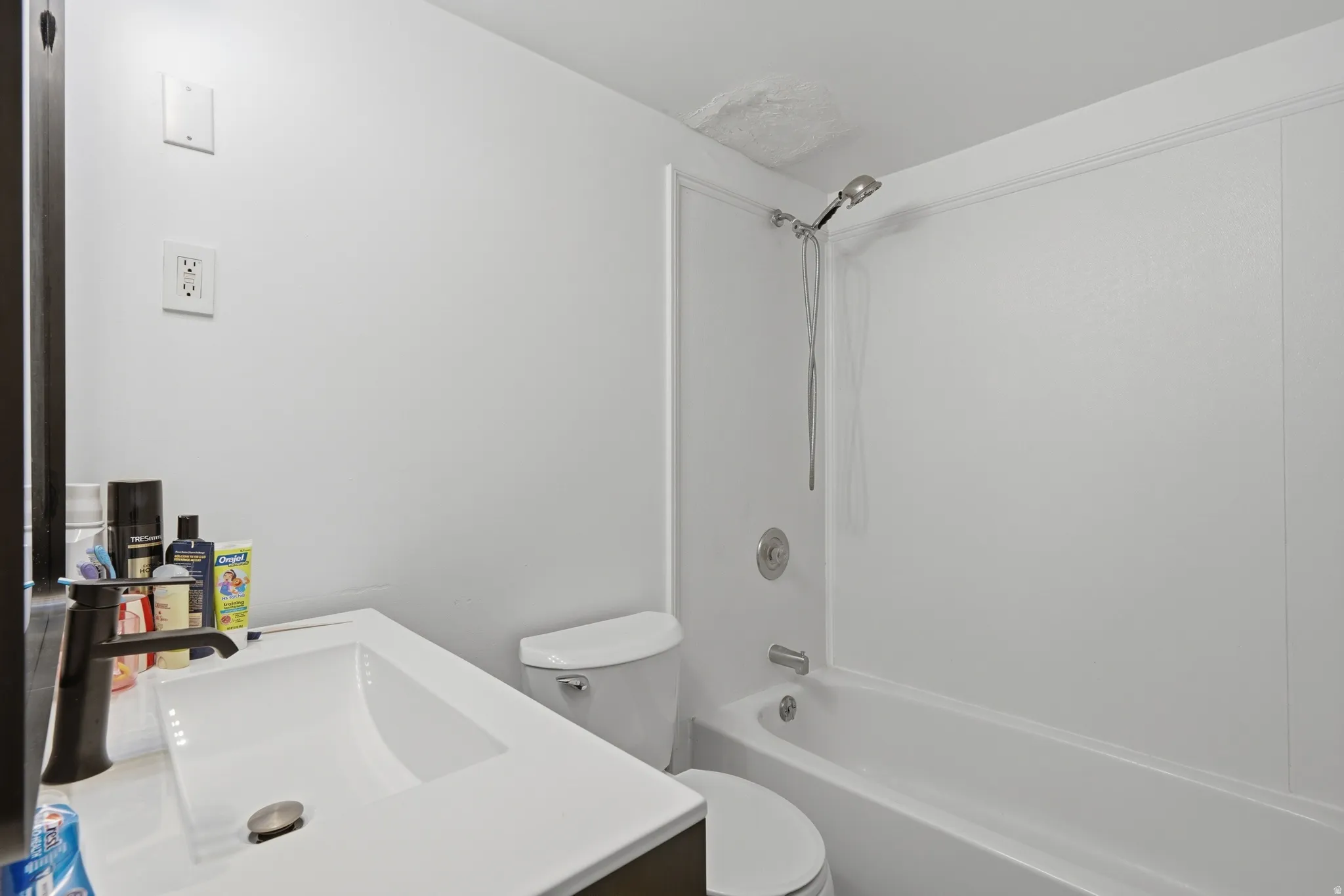 Bathroom featuring a white integrated sink with a dark bronze faucet, a white toilet, and a white tub with shower