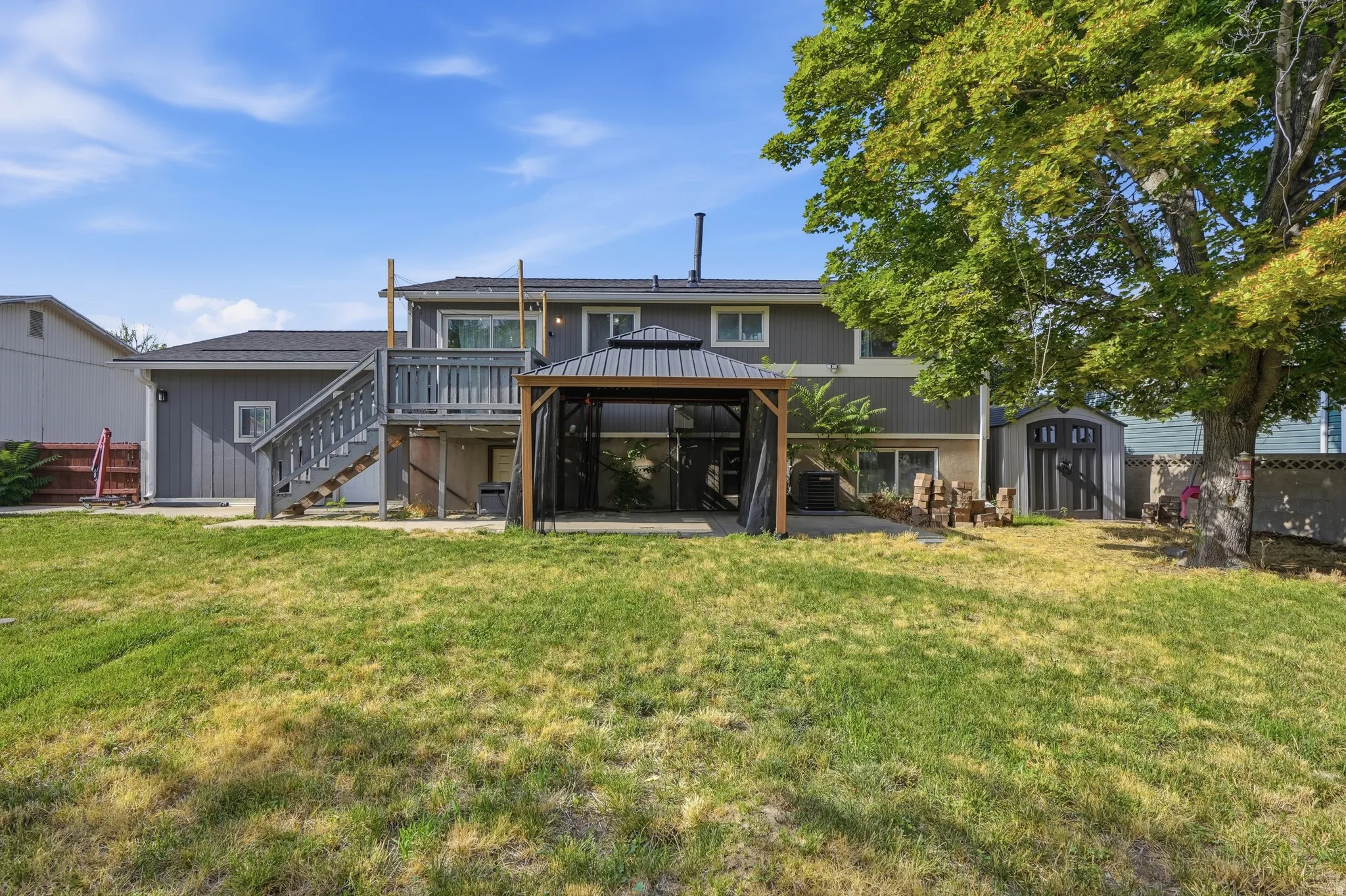 Spacious backyard featuring a substantial lawn area, a screened gazebo with a metal roof, and an elevated wood deck with stairs