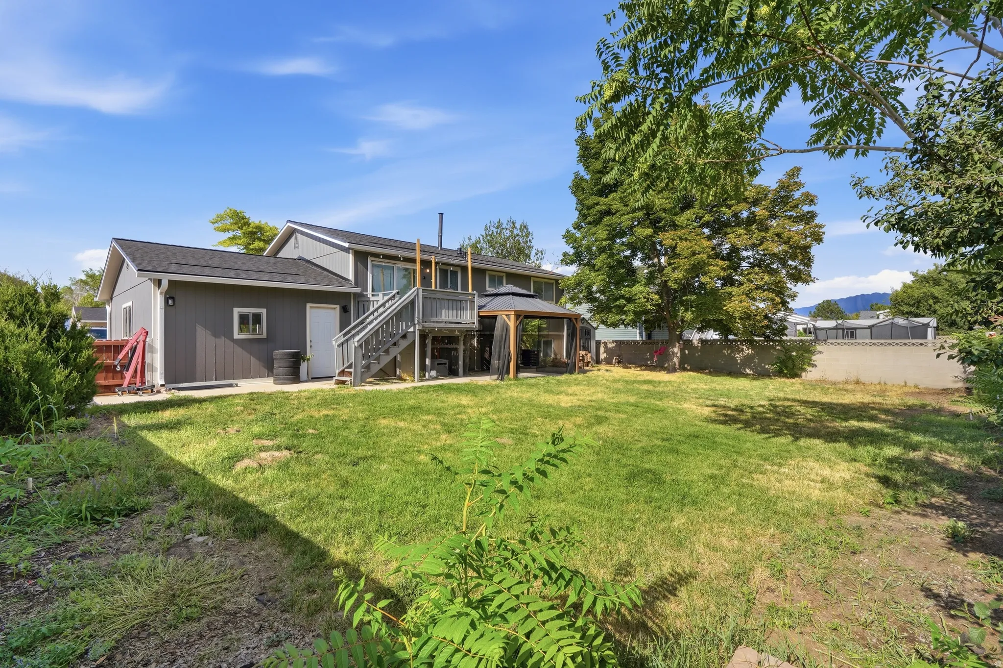 Expansive backyard with mature landscaping and level lawn space, complemented by a two-story residence featuring a covered deck, exterior stairs, and mixed siding materials