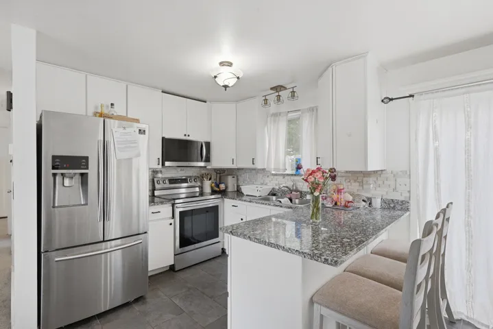 Kitchen featuring white cabinetry, stainless steel appliances, speckled countertops, a tile backsplash, and dark tile flooring