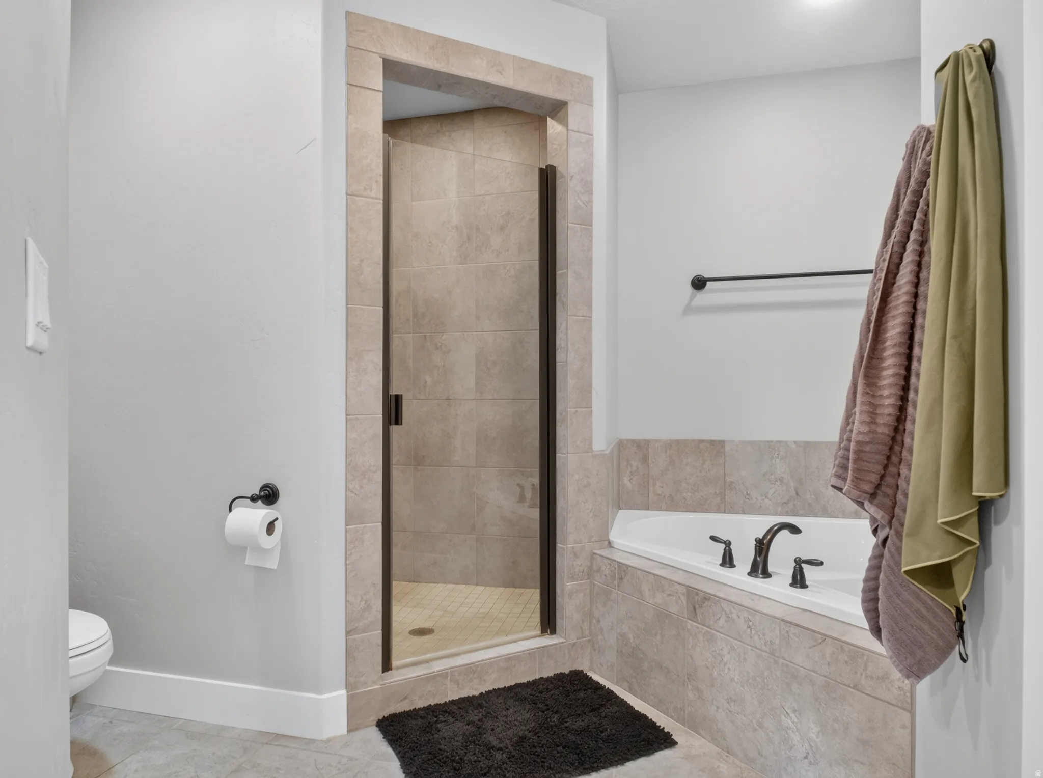 Tiled shower with a glass door, corner soaking tub, and matching dark bronze fixtures