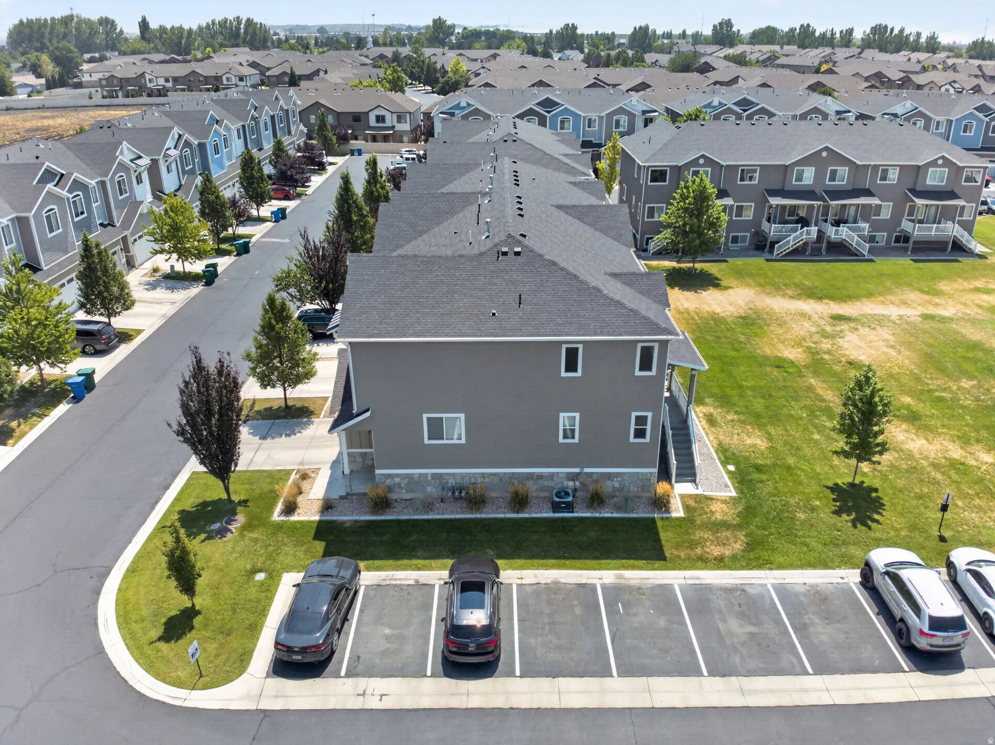 Contemporary townhouse with gray siding and stone accents, featuring a dedicated parking area, manicured landscaping, and a spacious grassy area to the side