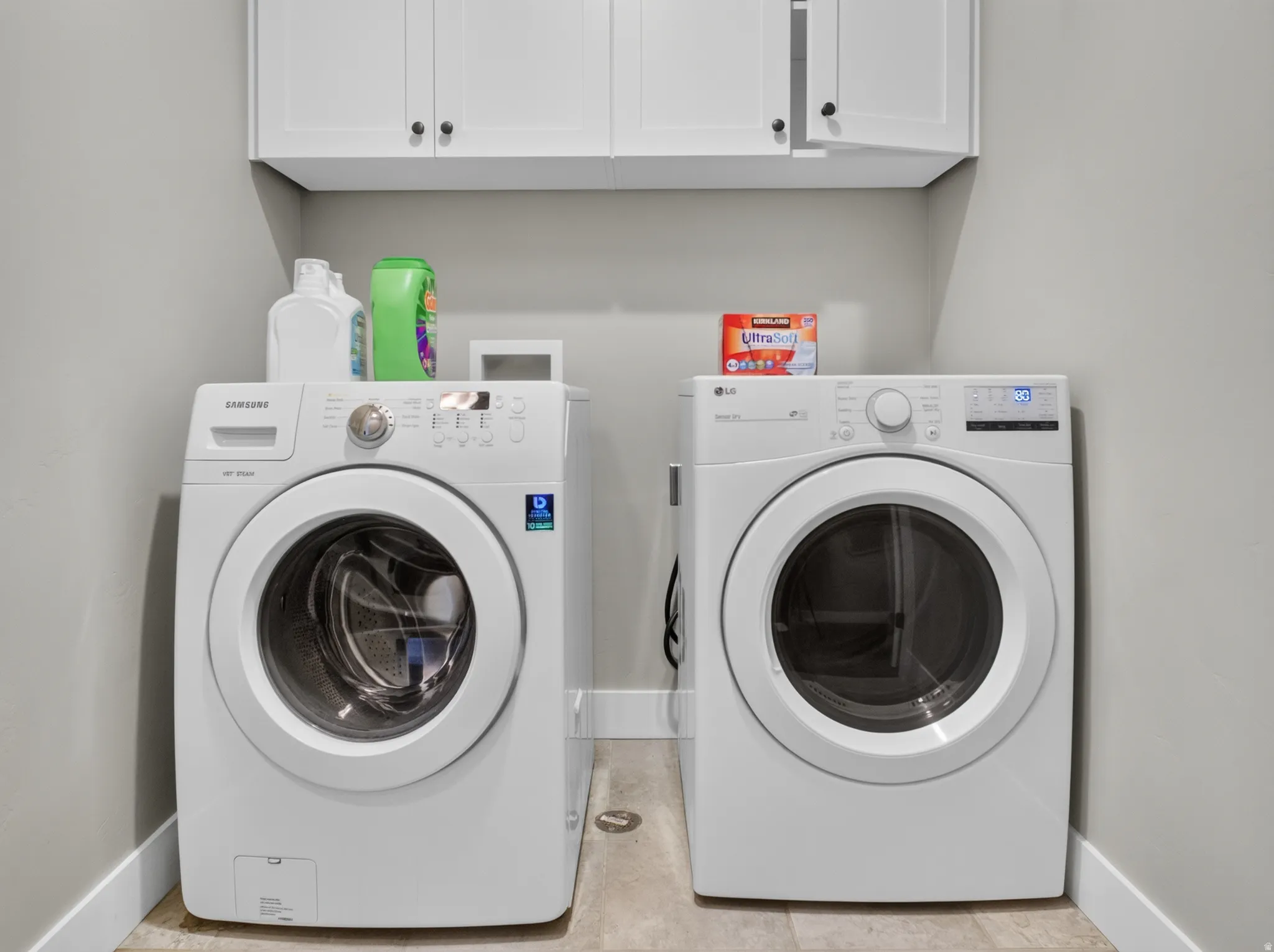 Laundry area featuring overhead white cabinetry with dark hardware, light gray wall paint, and light-toned flooring