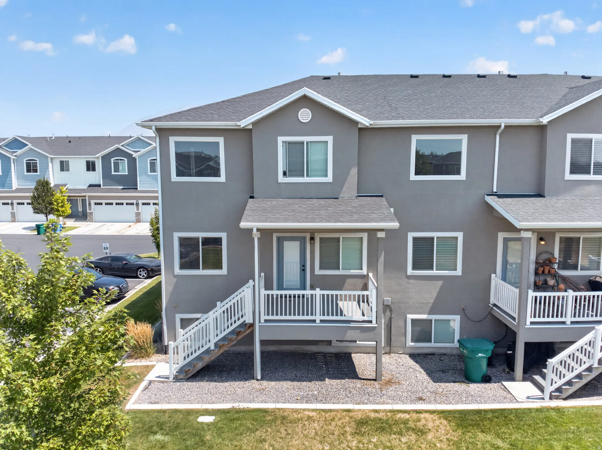 Rear exterior featuring a covered deck with white railings, a lower-level patio area, and a grey shingle roof