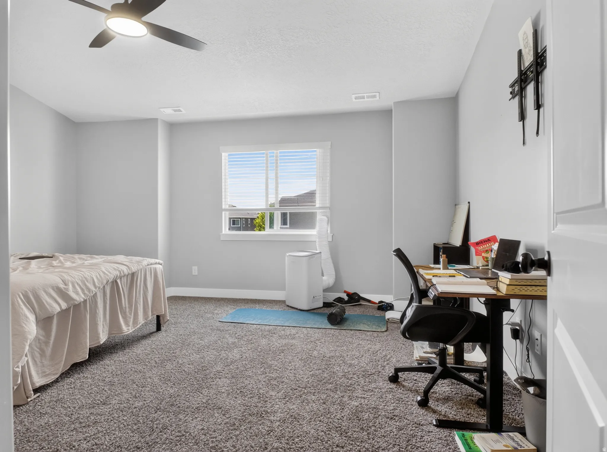 Well-lit room featuring light gray wall paint, gray carpet flooring, a window with horizontal blinds, and a built-in ceiling fan with light fixture
