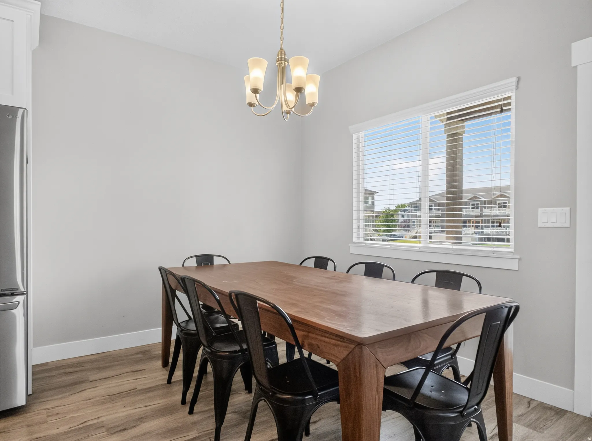 Dining area featuring wood-finish flooring, a large window with white blinds, and a brass-tone chandelier