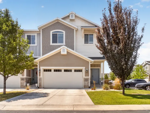 Multi-level residence featuring a two-car garage, stone accents, shingle siding, and a light-colored front door