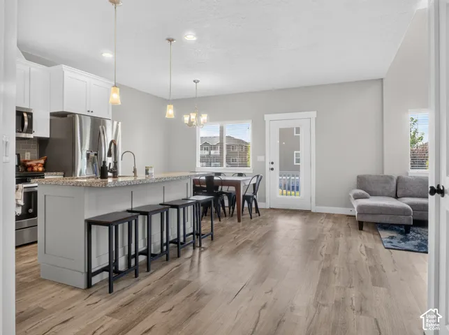 Open-concept living area featuring wood-finish flooring, a kitchen island with stone countertop, stainless steel appliances, a dining area with chandelier lighting, and a glass-paneled exterior door