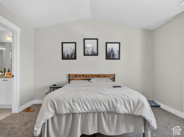 Neutral-toned bedroom featuring vaulted ceilings and textured carpeting