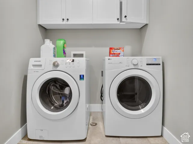 Laundry area featuring overhead white cabinetry with dark hardware, light gray wall paint, and light-toned flooring